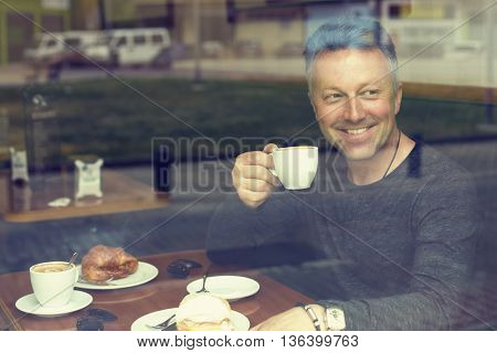 Attractive smiling mid adult man drinking morning coffee in cafe, image toned.