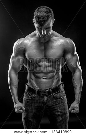 Muscular bodybuilder guy doing posing over black background. Naked torso in jeans. Black and white, b w