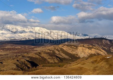 Scenic view with the beautiful mountains with snow and glaciers and the valley in the sunlight against the blue sky and clouds at dawn
