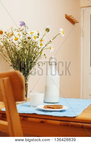 Simply stylish wooden kitchen with bottle of milk and glass on table, summer flowers camomile, healthy foog moring concept noone