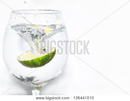 Slice of lime being dropped into a glass on white background on left hand side
