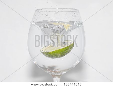 Slice of lime being dropped into a glass on white background