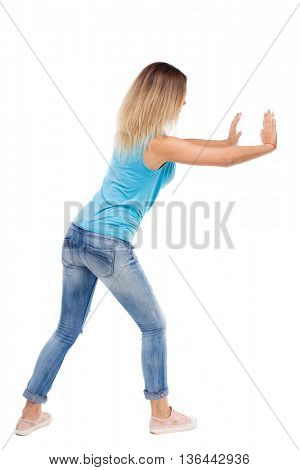 back view of woman pushes wall.  Isolated over white background. Rear view people collection. backside view of person. blonde in a blue shirt and jeans pushes something on my own.