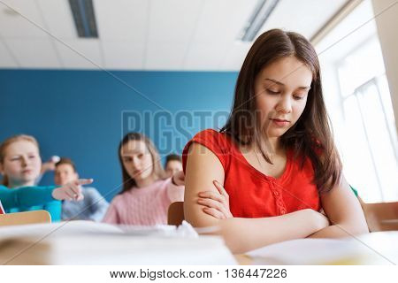 education, bullying, conflict, social relations and people concept - students teasing and judging girl classmate behind her back at school