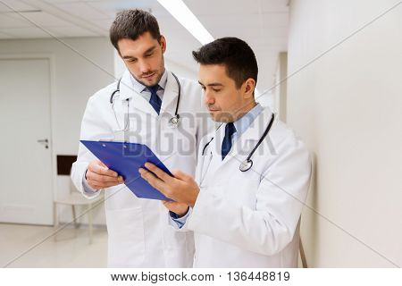 medicine, healthcare and people concept - two male doctors with clipboard at hospital corridor