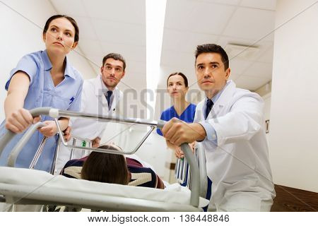 profession, people, health care, reanimation and medicine concept - group of medics or doctors carrying unconscious woman patient on hospital gurney to emergency