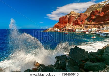 The waves beat against the rocks on a sunny summer day at Old port Ammoudi of Oia village at Santorini island in Aegean sea, Greece