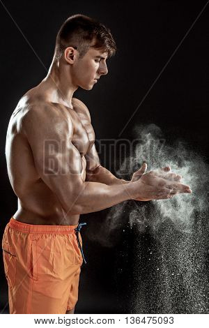 young muscular man preparing to hand lifting heavy weight. White talcum dynamically scatters in different directions. stands sideways