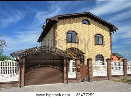 Two-storeyed yellow brick cottage with white concrete fence and metal gate sunny summer day