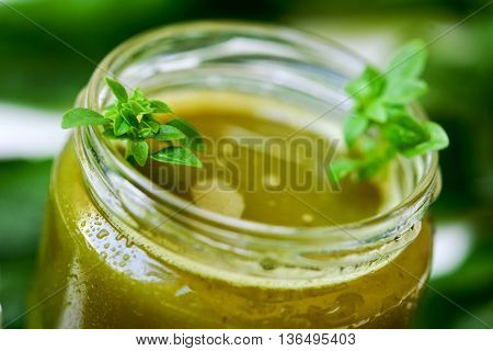 closeup of a green detox smoothie served in a glass jar with some leaves of basil