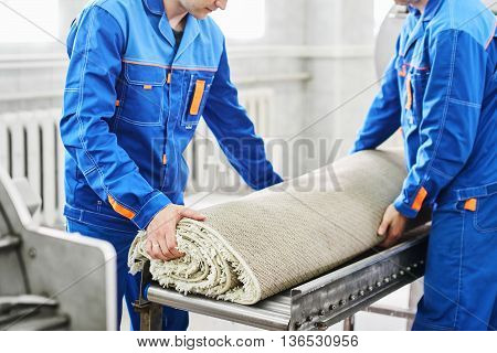 Men workers cleaning get carpet from an automatic washing machine and carry it in the clothes dryer in the Laundry room