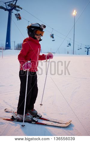 Girl in helmet with camera skiing on snowy slope at ski resort in evening. 
