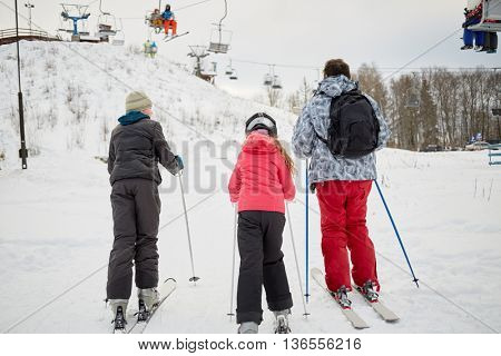 Man with two children ski to cableway in winter day at ski resort, rear view.