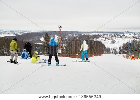 People equipped for skiing and snowboarding on the top of snowy slope.