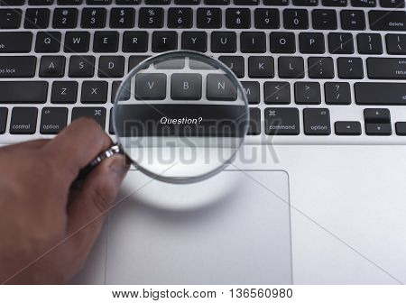 Hand holding magnifying glass with Question? word on black keyboard with copyspace area.