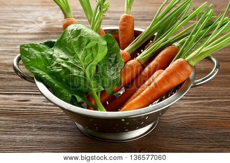 Carrots with sorrel in colander on wooden table
