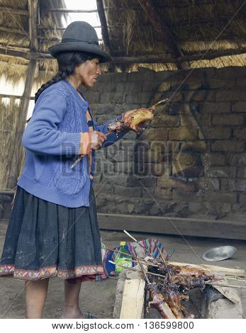 October 22 2012 - Paru Paru, Peru: Native Peruvian woman preparing guinea pigs over fire. Guinea pigs are special dish in Peru prepared for weddings and religious ceremonies.