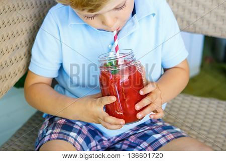 Adorable little kid boy drinking healthy fruits and vegetables juice smoothie in summer. Happy child enjoying organic drnk.