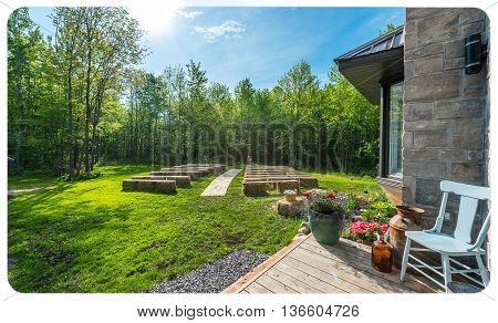 Springtime woodlot lawn of baskets, wagon wheels, a chair, hay benches, flowers, decorations & sunny day comprise an outdoor country, back yard wedding setting.