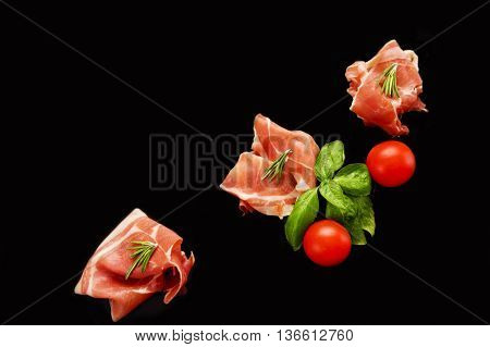 sliced prosciutto isolated on black background. Italian appetizer.