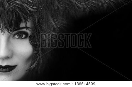 Close-up portrait of mysterious young beautiful woman with black feather headdress on black background with copy space. Model fashion shooting. Smoky eyes make-up. Sensual lips. Perfect pure skin. Femme fatale. Retro style. Vintage style. Cabaret girl. Bl