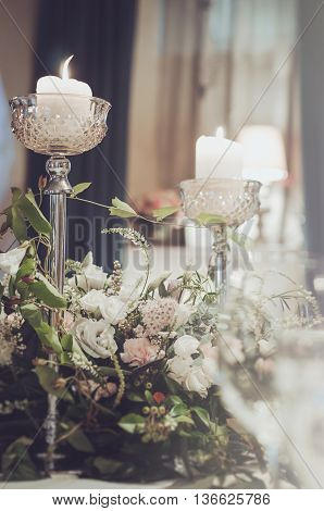Luxury banquet table set with rich decoration of flowers cream roses pink carnation white eustoma with high elegant candle coasters glass goblets for wine or champagne on tablecloth. in restaurant. Wedding concept. Floral arrangement. Copy space text here