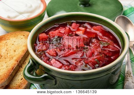 Borscht - traditional russian and ukrainian beetroot soup in green ceramic pot on wooden background.