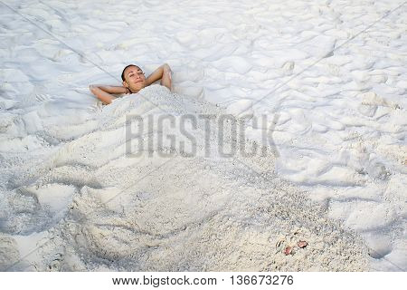 The girl lies on a white sand buried in the sand. Relax and enjoy a beach holiday.