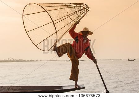 INLE LAKE MYANMAR - JANUARY 14 2016: Unidentified Burmese fisherman on bamboo boat catching fish in traditional way with handmade net. Inle lake Myanmar Burma