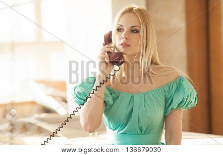 pretty blonde woman in green dress talking on old telephone. Fashion model. Sunny color.