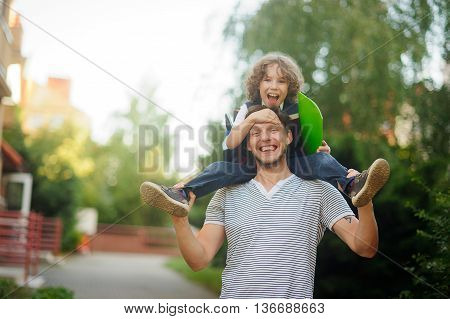 Little schoolboy sitting on the shoulders of his father. The father holds the boy's legs. The boy delighted. He likes to joke with dad. Father and son smiling happily. Back to school