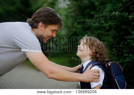 The father sees off the son-schoolboy in school. It has bent to the boy and has taken it for shoulders. The father and the son look against each other with love and smile.