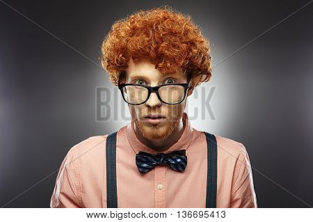 Red Hair Models. Bearded man. Portrait. Young Redhead man curly in glasses, bow tie and suspenders on gray background.