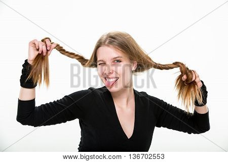 blonde girl holding her hair in his hands and smiling showing tongue. Studio, white background.