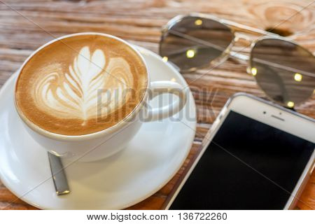 cup of the latte art coffee with spoon and plate on the brown bark beautiful texture background with warm light decorated with sunglasses