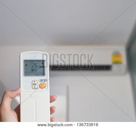 Left hand holding remote air conditioner turn up to 26 celcius with air conditioner blurred background