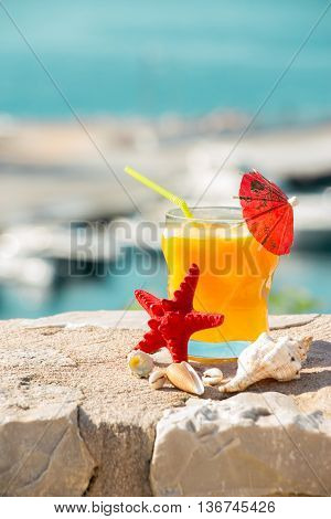 Right a glass of fresh orange juice next to shells to the left the empty space on the background of the sea. Orange juice sea and seashells. Vertical. Daylight.