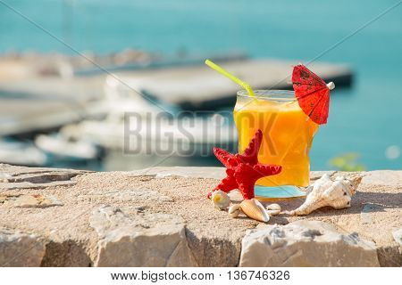 Right a glass of fresh orange juice next to shells to the left the empty space on the background of the sea. Orange juice sea and seashells. Horizontal. Daylight.