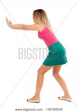 back view of woman pushes wall. Isolated over white background. Rear view people collection. backside view of person. Blond girl in a green skirt pushing something heavy right.