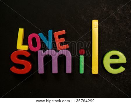 Love and smile! Inspirational message in vibrant colorful magnet letters on black background