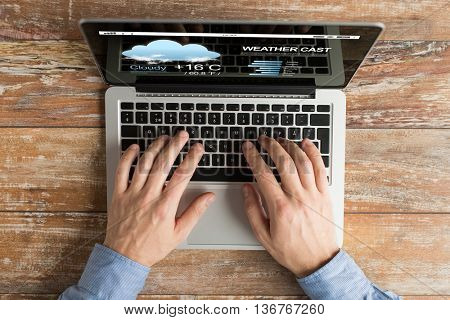 business, weather cast, people and technology concept - close up of male hands typing on laptop computer with meteo forecast on screen on table