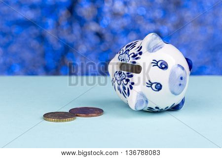 White piggy bank on a blue background: it's on its side with a few penny's, a concept of a tight budget