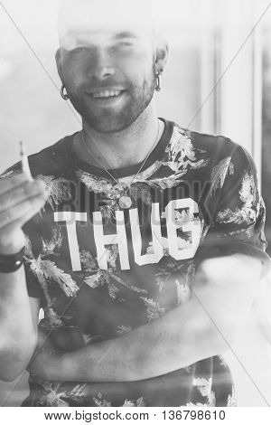 Portrait of a young fashionable blond man smoking, looking to the camera. Weating t-shirt, black and white photo