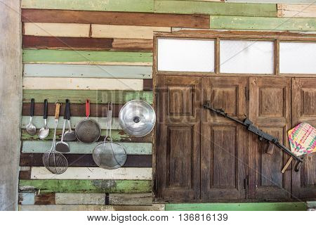 a lot of cooking instruments hang on the wooden wall near the windows and the old gun
