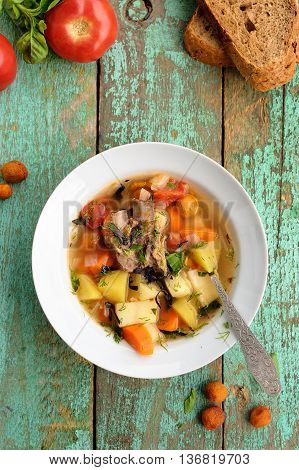 Homemade chorba soup with lamb meat on bone potato carrots bay leaf and dried apricots served with basil and tomatoes overhead view