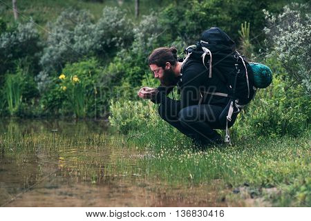 Hiker With Backpack Drinking Watr From Lake
