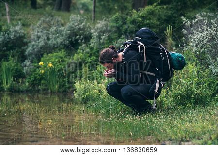 Hiker With Backpack Drinking Watr From Lake