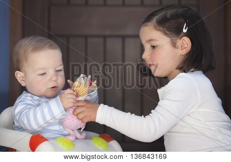 Toddler girl offering to his brother a doll. Overcoming sex stereotyping boundaries