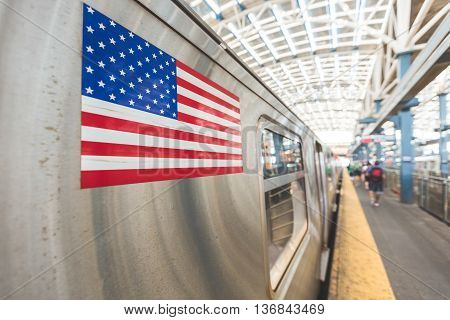 United States flag on a subway train in New York. There are some unrecognizable and blurred persons on the platform waiting to board. Transport and travel concepts. Focus on the flag