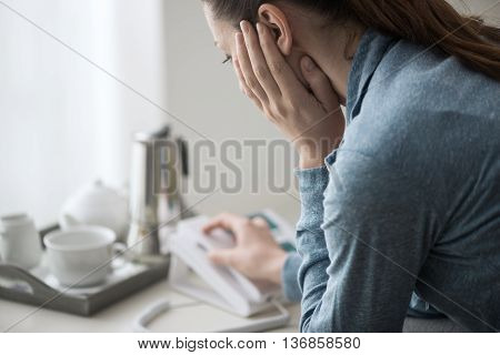 Sad depressed woman at home sitting on the sofa she is calling an help line with her phone